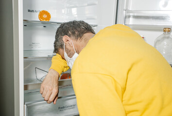 Hungry man in mask leaning on refrigerator