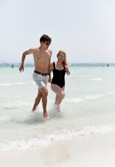 Two young people holding hands run out of the sea