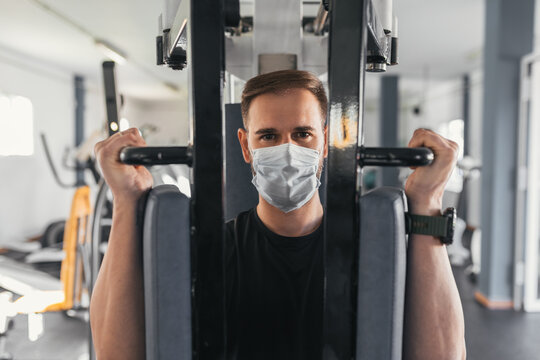 Young man using gym machine with mask. Coronavirus. Sport and health concept.