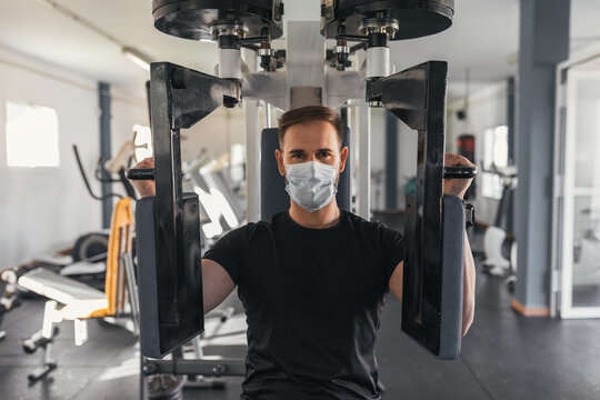Young man using gym machine with mask. Coronavirus. Sport and health concept.