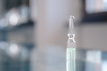 Ampoule flask with vaccine on glass surface backdrop. Dose of vaccine. Mock up. Text space. Bokeh and reflect