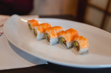 Close-up salmon sushi uramaki roll on decorated plate in a restaurant. Japanese healthy food concept.