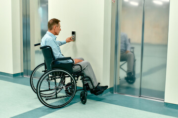 An elderly disabled man in a wheelchair presses the call button for the elevator in a modern clinic.