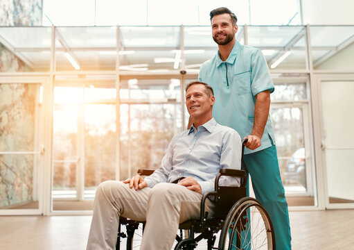 A young handsome doctor with his elderly disabled person in a wheelchair walk the corridors of a modern clinic.