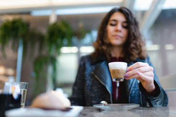 Close-up young caucasian woman in a cafe sitting in a table holding a cup of espresso coffee.