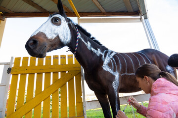 Girl with watercolors paints a skeleton on a horse to celebrate Halloween
