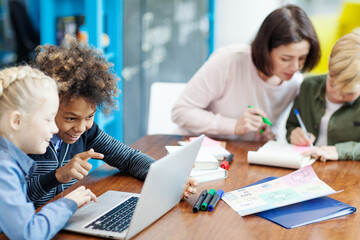 Two elementary school kids, boy and girl, having fun browsing through pictures on laptop computer...