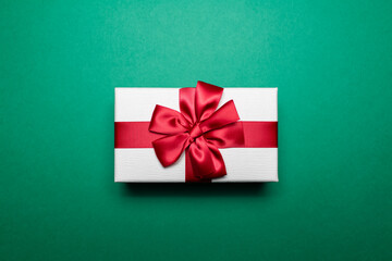 Close-up of white gift box with red ribbon bow on background of  green color.