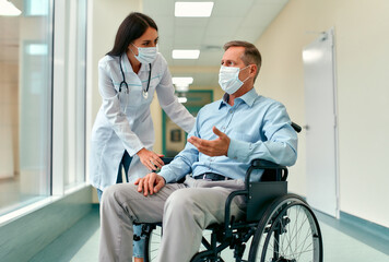 Caucasian nurse taking care of a mature male patient sitting in a wheelchair at the hospital. A...