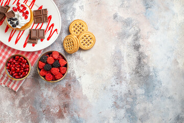 top view cake with chocolate on oval plate bowls with pomegranate raspberry candies biscuits kitchen towel on marble ground with copy space