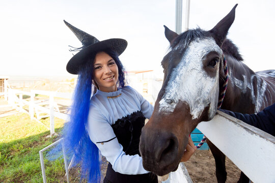 A girl dressed as a witch shows the face of a horse painted with white paint for the holiday of halloween