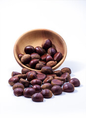 Chestnuts spilled from wooden bowl on white background. Castanea sativa, sweet ripe Chestnuts