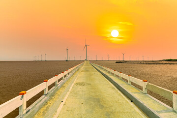 Clean energy, wind power plant in sunset sky with a pathway to the giant wind turbines at sea to provide electricity for human life.