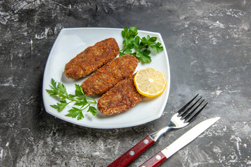 bottom view cutlets lemon slice parsley on white plate fork and knife on grey background with copy...