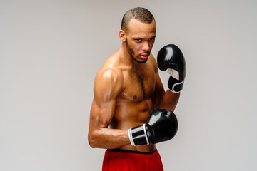 Confident young African boxer in boxing gloves standing over light grey background