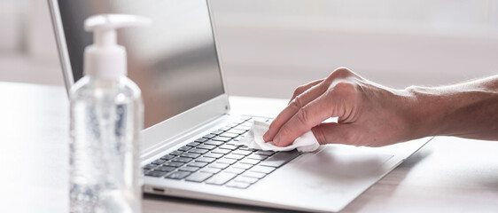 Woman disinfecting laptop keyboard; prevention of virus and bacteria infection