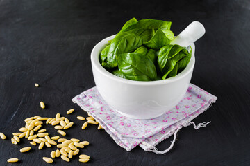 Ceramic mortar and pestle with green basil leaves, on gray background.