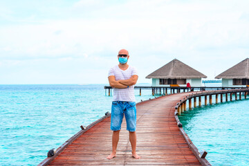 Fototapeta na wymiar a young man wearing a protective face mask stands on a pier near water villas in the Maldives, a concept of travel during the covid pandemic
