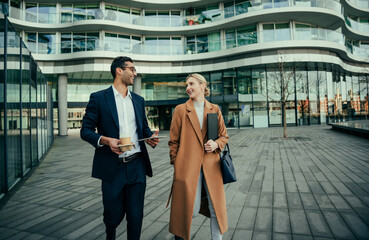 Two colleagues walking together to work discussing meetings while enjoying hot coffee