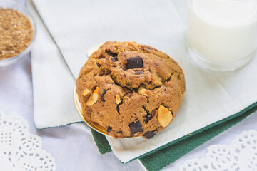 Close up high angle view chocolate chip cookies on a white table with a cup of milk in brown sugar background