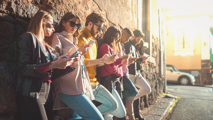 Generation y young people addicted by smart phones, internet and social media application. Multiracial friends standing on a wall holding and using their smartphone watching content online. Filtered