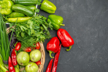 A vegetable basket with a bunch of green and peppers cucumber and tomatoes with stem on dark background close up view