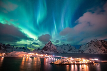 Aurora borealis on the Hamnoy village in Lofoten islands, Norway. Green northern lights above mountains. Night sky with polar lights. Night winter landscape.