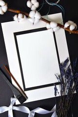 Background flatlay white frame and a sheet of paper on a black sheet with decor. Vertical