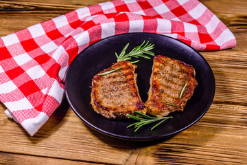 Plate with roasted steaks and rosemary twigs on a wooden table