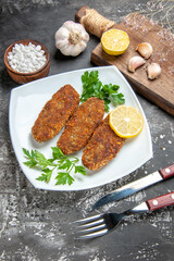bottom view cutlets lemon slices parsley on white plate fork and knife garlic bowl of sea salt cutting board on grey background