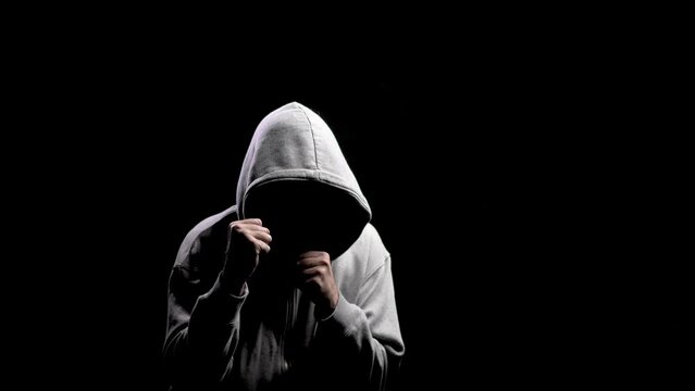 Hooligan wants to fight, to provoke. Silhouette of a man with a darkened face in a hood on a black background. A portrait of a murderer, a hacker.