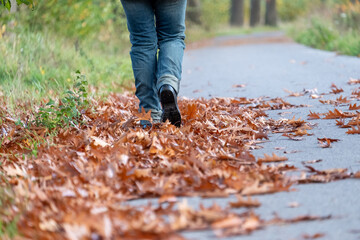Feet trekking boots hiking through fall foliage. Traveler alone outdoor wild nature. Woman walking away on the road covered with yellow brown leaves.Lifestyle Travel extreme survival concept. Autumn