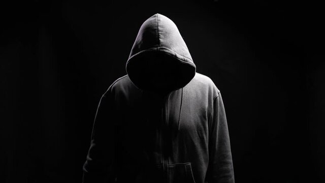 Fun psychopath with toys. Silhouette of a man with a darkened face in a hood on a black background. A portrait of a murderer, a hacker.