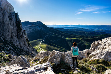 Rear view of unrecognizable carefree young woman on a mountain peak with backpack on shoulders...