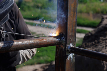 male welder welds iron parts at construction