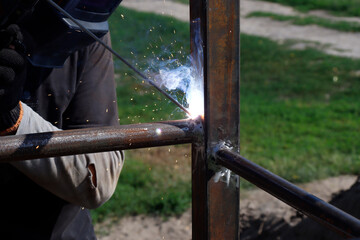 male welder welds iron parts at construction