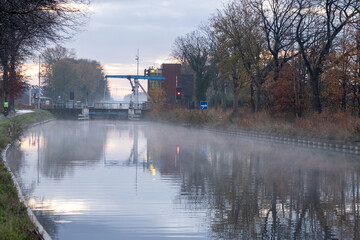 River stream canal bending with grass banks and wild flowers and trees in a scenic landscape on a misty autumns morning sunrise day. High quality photo