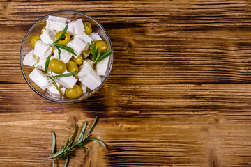 Chopped feta cheese, rosemary and olives in glass bowl on a wooden table. Top view