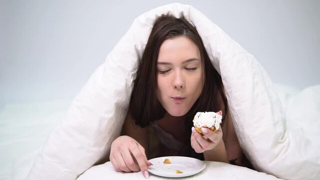 Young woman happily eats a&nbsp;cake shows the fuck