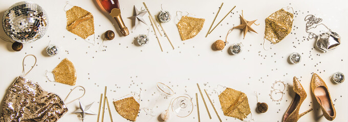 Flat-lay holiday party frame with Discoball, glitter face masks, traditional golden and silver glitter decorations, shoes, dress, bag and champagne bottle over white background, top view, copy space © sonyakamoz