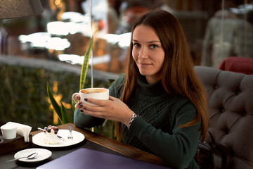 young brunette woman drinking coffee in a cafe and eating dessert