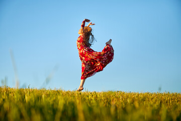 Beautiful woman or girl with magnificent figure and plastic movements walking and dancing in green field with trimmed grass in the setting sun during sunset with warm yellow light.