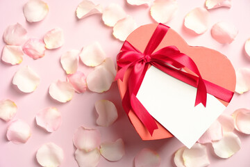 Heart shaped box with blank greeting card and rose petals on pink background. Valentine's day, Mother's day, anniversary concept.