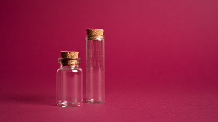 Two small decorative bottles with cork. Empty vial necklace on magenta background. Tiny glass jars different size