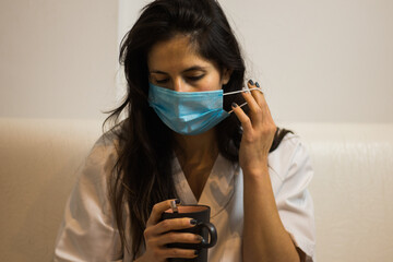 Mujer enfermera descansando en un sofá con una taza y mascarilla coronavirus.