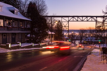 Dusk street view of light trails of cars speeding by in the Cap-Rouge area with the 1908 trestle bridge and the St. Lawrence River in the background, Quebec City, Quebec, Canada