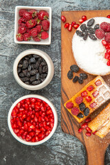 top view waffles with berries on cutting board bowls with raspberries raisins pomegranates on grey-white background