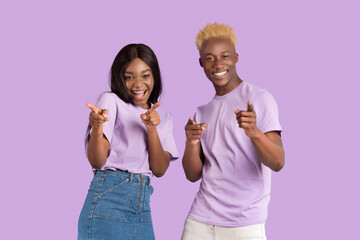Portrait of cheerful black couple pointing at you over lilac studio background