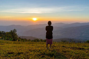 Fototapeta na wymiar Young woman traveler looking at the sunrise over the mountain