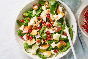 Fruits salad with nuts, balanced food, clean eating. Spinach with apples, pecans and feta, garnished with pomegranate seeds in bowl on table with white tablecloth. - Powered by Adobe
